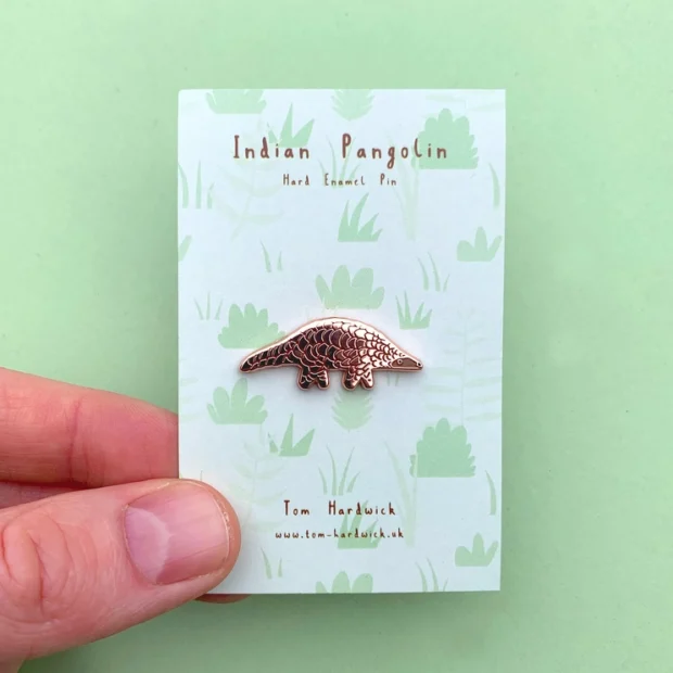 Indian Pangolin enamel pin badge on a beautiful backing , card of green folage.